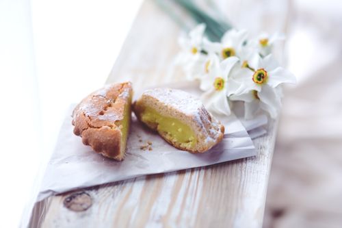 Free A half-eaten lemon tart on a rustic wooden table, with daffodils in the background. Stock Photo