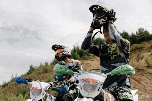Free Two riders on dirt bikes preparing for an off-road motocross adventure under a cloudy sky. Stock Photo
