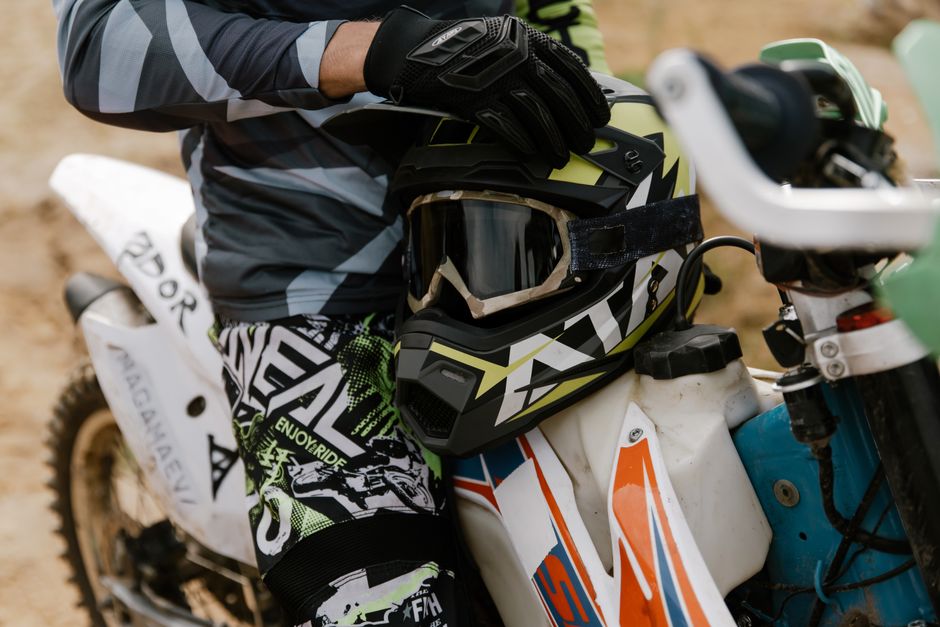 A motocross rider holding a helmet, standing beside a dirt bike, ready for an adventure.
