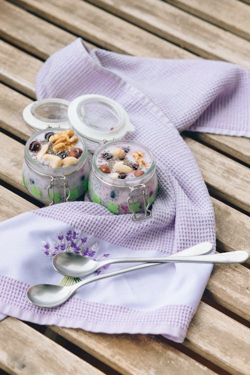 Delicious Desserts in Glass Jars Beside a Pair of Spoons and Textile
