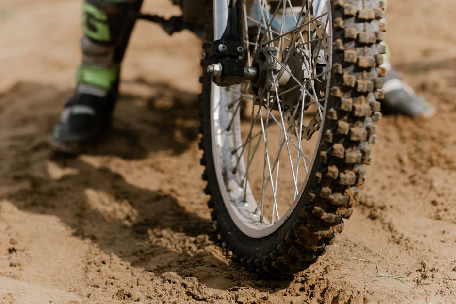 Detailed view of a muddy off-road motorcycle tire in action on a sandy terrain.