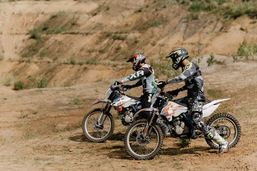 Free Two dirt bikers equipped with helmets prepare for a ride on a sandy outdoor trail. Enthusiastic and energetic. Stock Photo