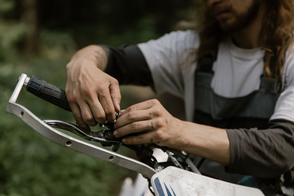 Adult male fixing a dirt bike handlebar in an outdoor setting, focusing on repair and maintenance.