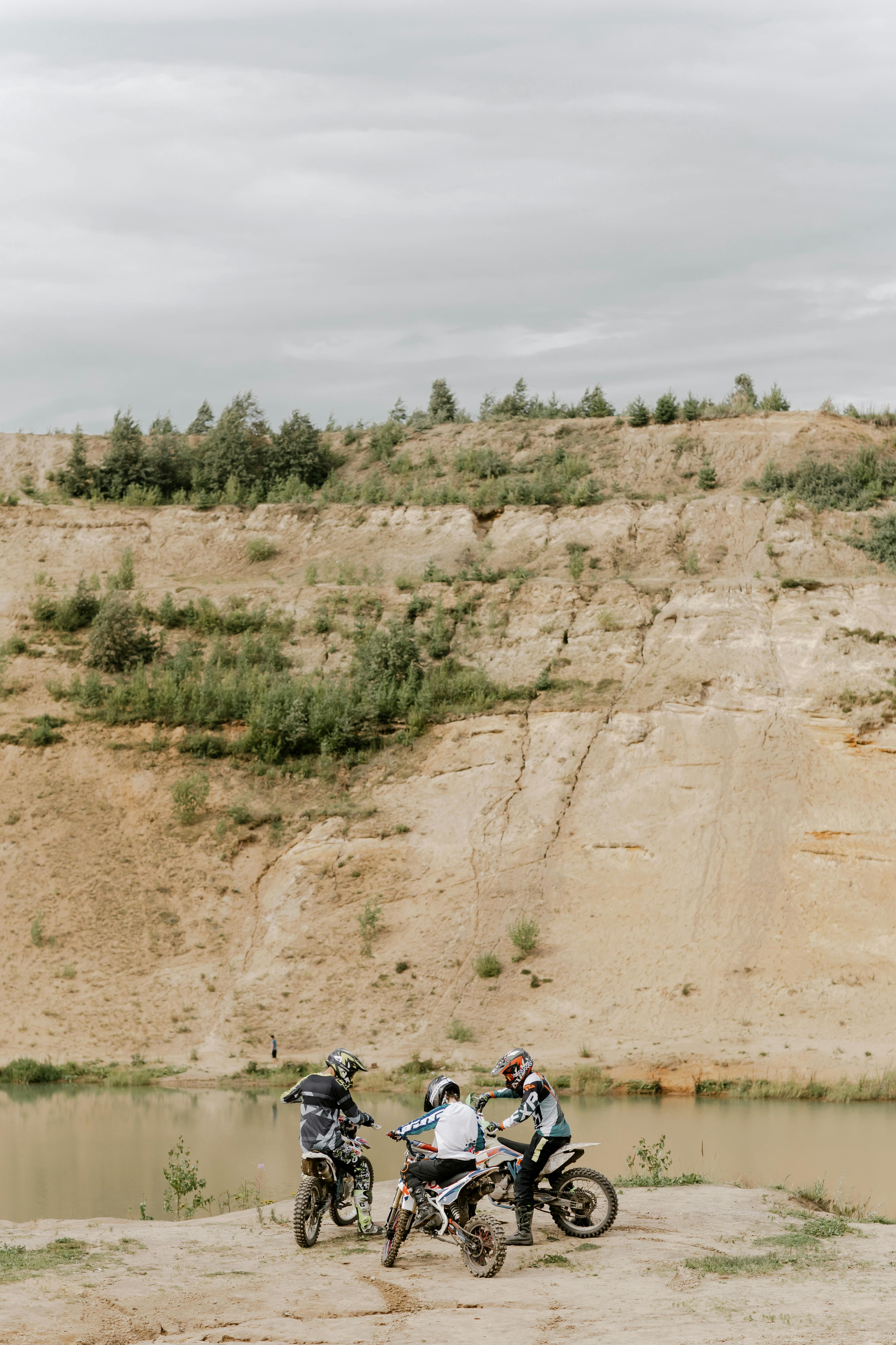 Three motocross riders pause near a scenic lakeside cliff, capturing the spirit of adventure and off-road exploration.