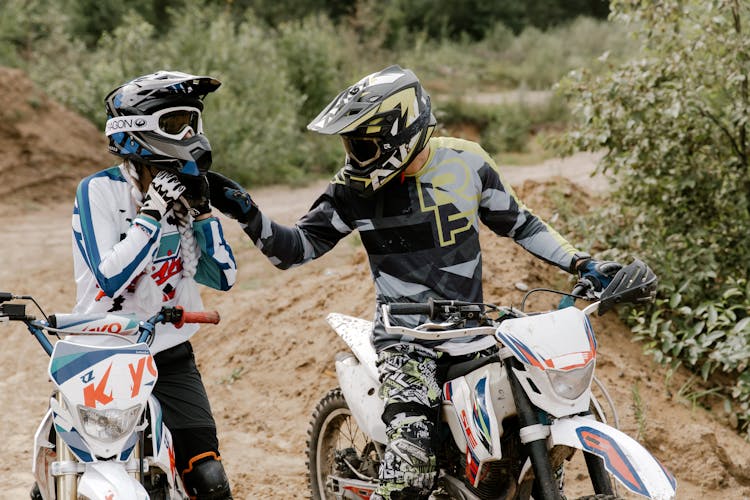 Two People In Motorcycle Suits Riding On Motocross Dirt Bikes