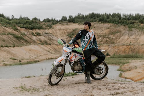 Free Man in Black Long Sleeve Shirt Leaning on a Dirt Bike Stock Photo