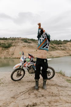 A biker adjusts gear on a dirt path by a scenic lake, ready for off-road adventure.