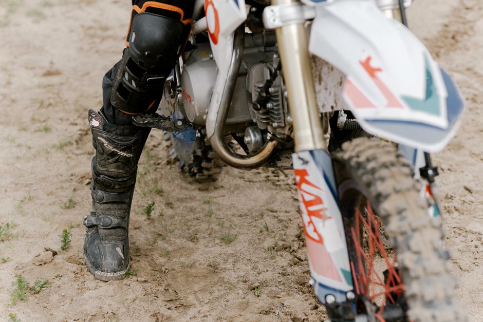 Detailed view of a dirt bike and rider's gear on a sandy trail, showcasing adventure sports.