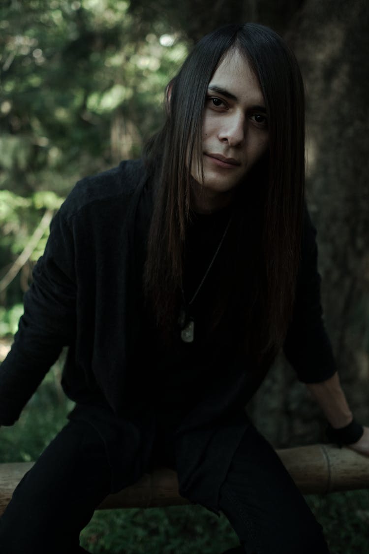 Man With Long Black Hair Sitting On Fence