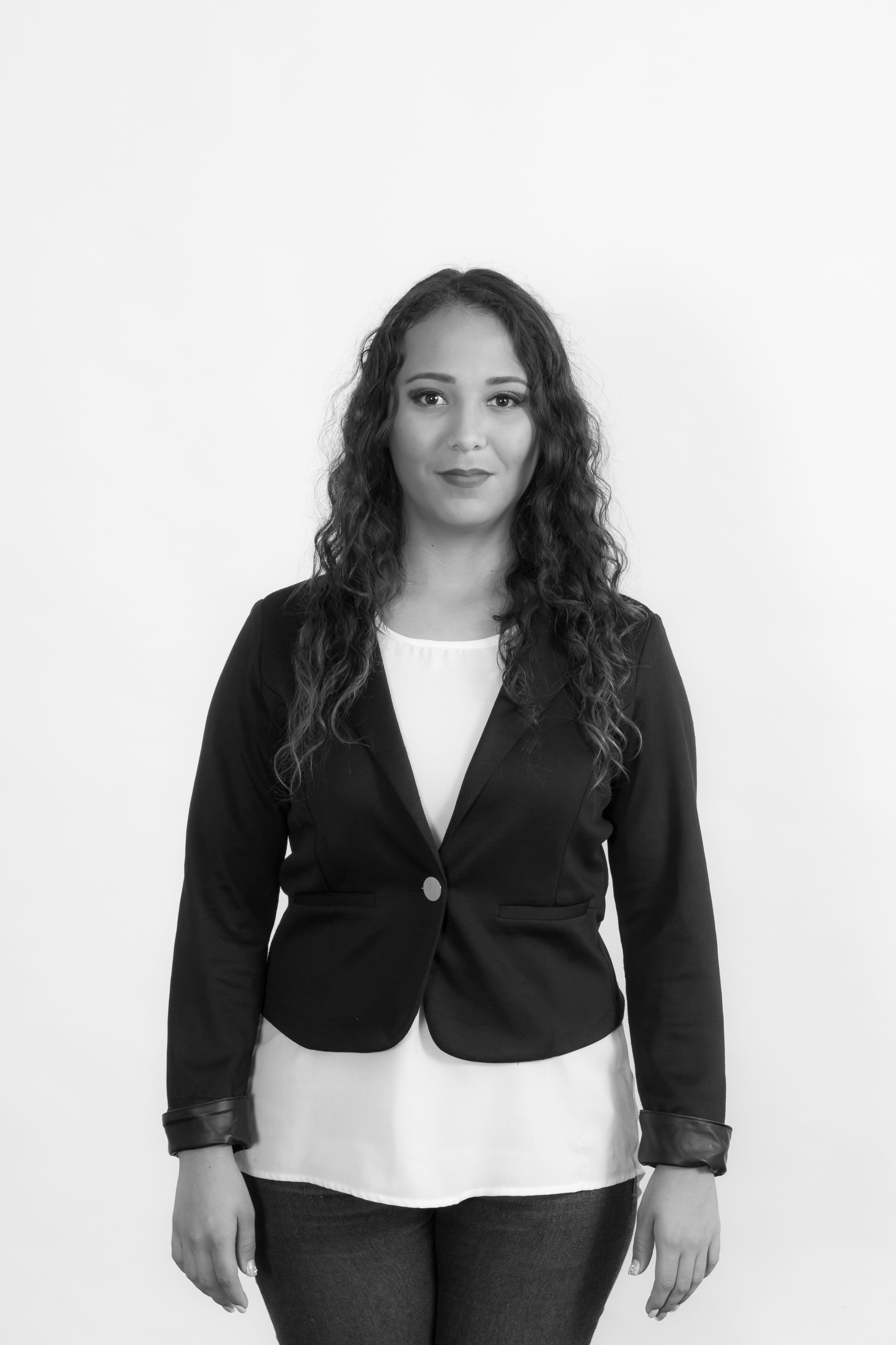 Black and white portrait of a confident young woman in a blazer, looking directly at the camera.