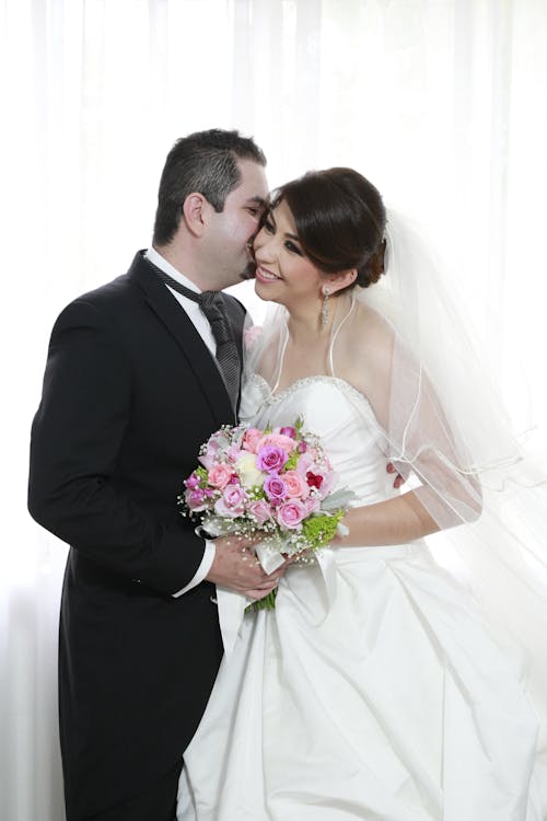 Man in Black Suit Kissing Woman in White Wedding Dress