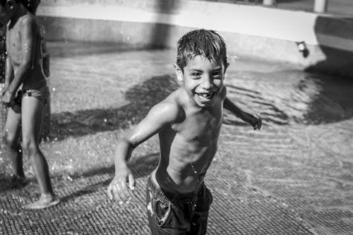 Grayscale Photo of Smiling Boy Playing on a Fountain