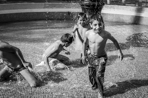 Grayscale Photo of Kids Playing on a Fountain