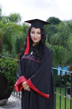 一位年轻女子身穿学术礼服，在户外摆姿势庆祝毕业