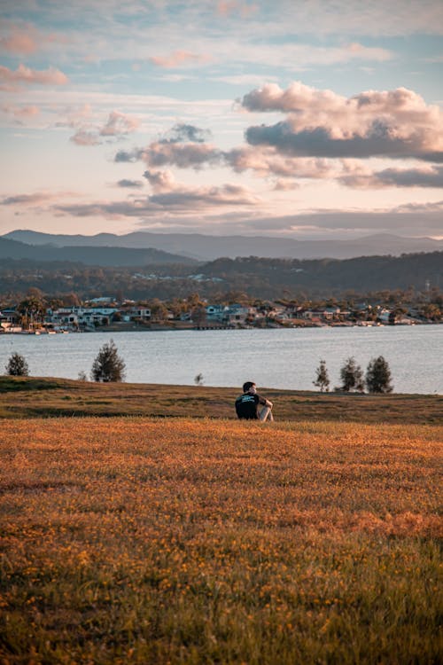 A Man Sitting on a Grassland Near a Lake