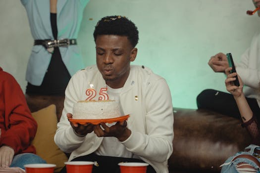 A young adult man blowing out candles on a birthday cake at a party.