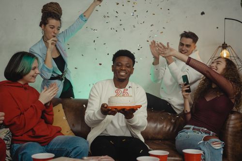 Free A diverse group of friends celebrates a 25th birthday indoors with cake and confetti. Stock Photo