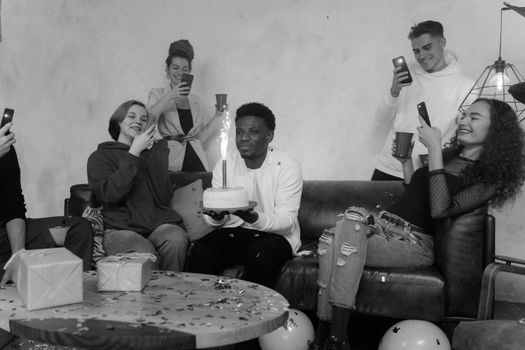Black and white photo of diverse friends celebrating a birthday indoors.