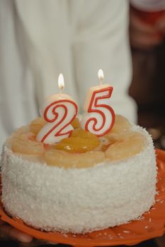 A close-up of a 25th birthday cake with lit candles and fruit topping. Ideal for celebrations.
