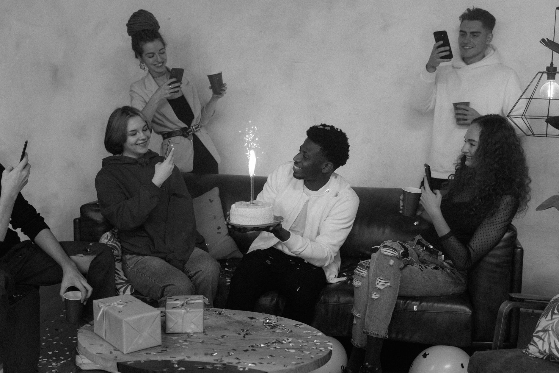 A diverse group celebrating a birthday party indoors with cake and presents.
