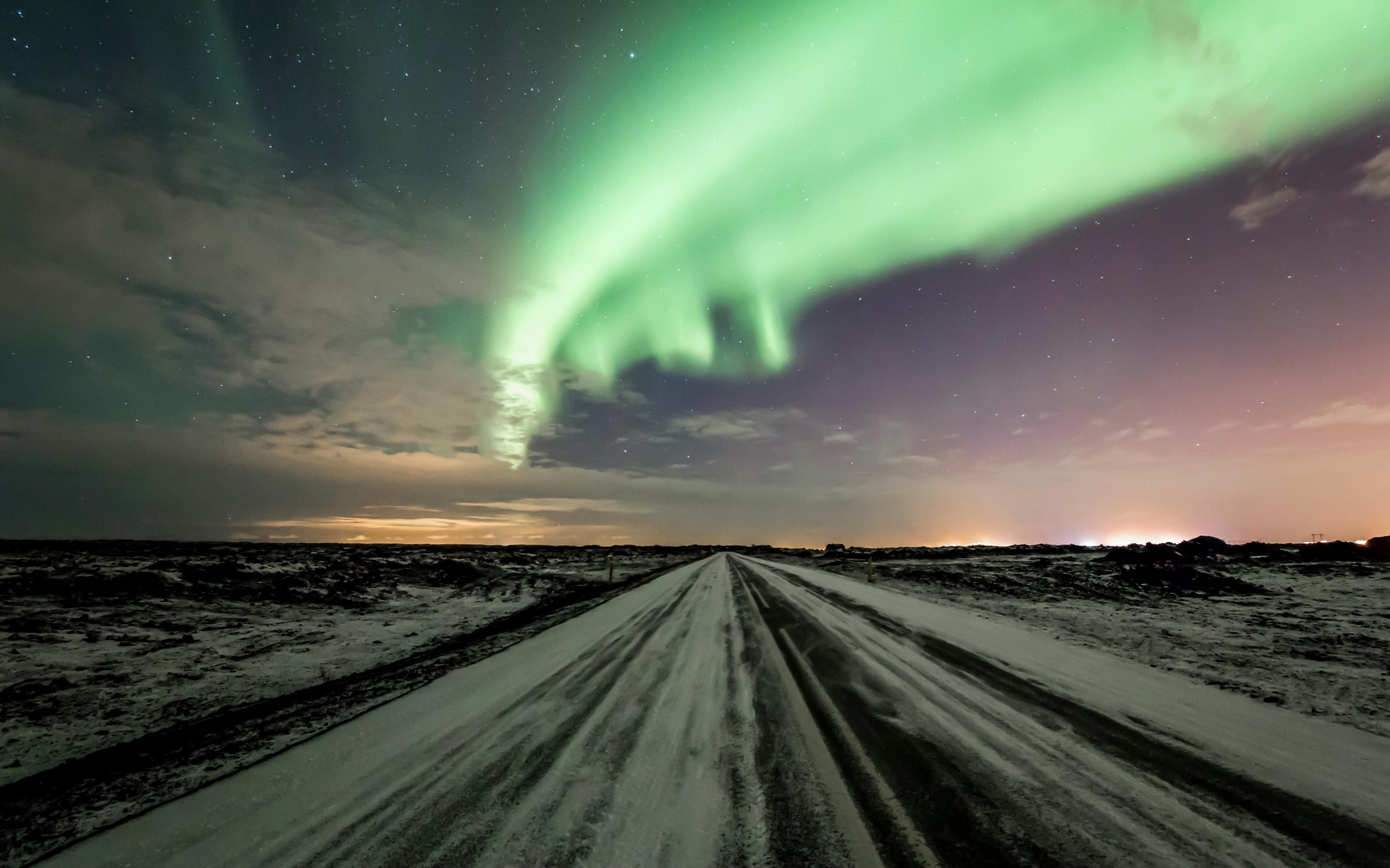 Stunning northern lights display over a snowy road in Iceland, enhancing the magical night sky.