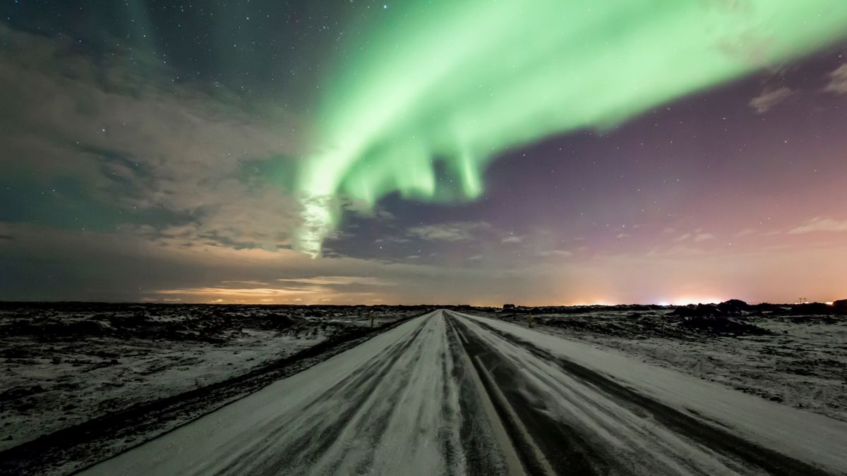 아이슬란드 오로라 시즌 — Stunning northern lights display over a snowy road in Iceland, enhancing the magical night sky.