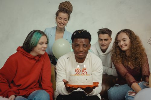 Free A joyful group of friends celebrating a 25th birthday indoors with a cake and candles. Stock Photo