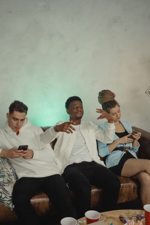 Free Three friends celebrating on a couch with smartphones and party decorations. Stock Photo
