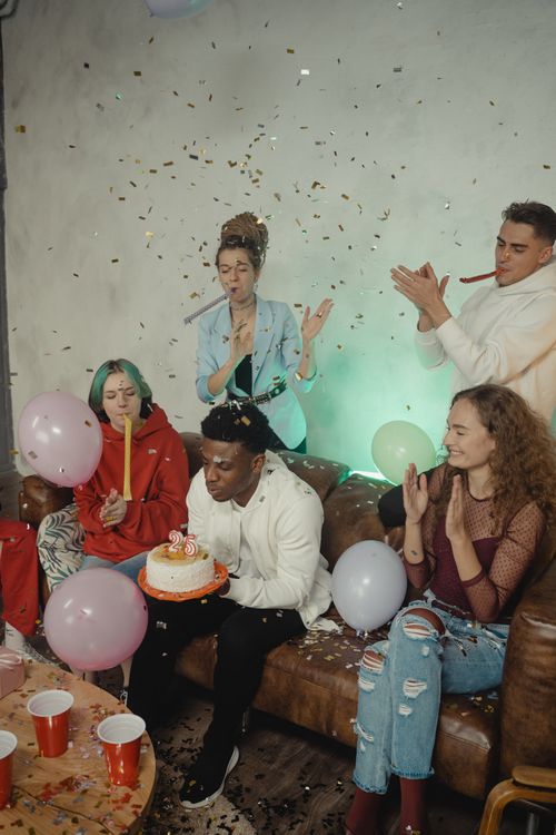 Free Group of young adults enjoying a vibrant birthday party with cake, balloons, and confetti indoors. Stock Photo
