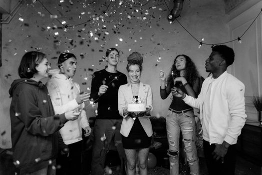 A joyful group celebrates a birthday with confetti and cupcakes indoors, capturing diversity and happiness.