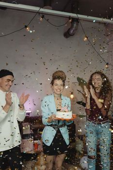 Group of young adults celebrating a 25th birthday with cake and confetti indoors.