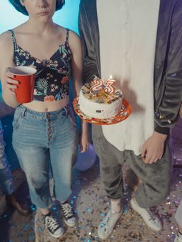 Group of friends holding a cake with candles celebrating a 23rd birthday indoors.