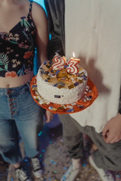 Free A Person Holding a Cake with Lighted Candles and Confetti on Top Stock Photo