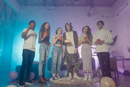 Group of diverse young adults enjoying a festive indoor party with decorations and drinks.