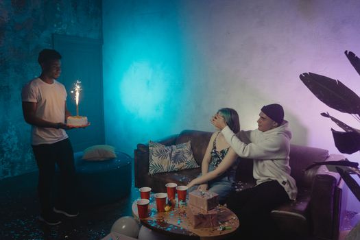 Young friends surprising a girl with a cake during an indoor birthday party.