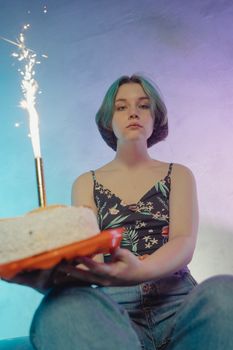Woman holding a cake with a sparkler, celebrating indoors with colorful lighting.