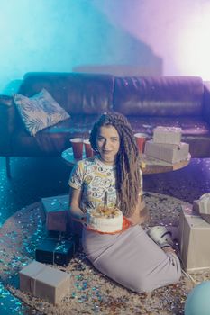A young woman enjoying her birthday surrounded by gifts and confetti indoors.