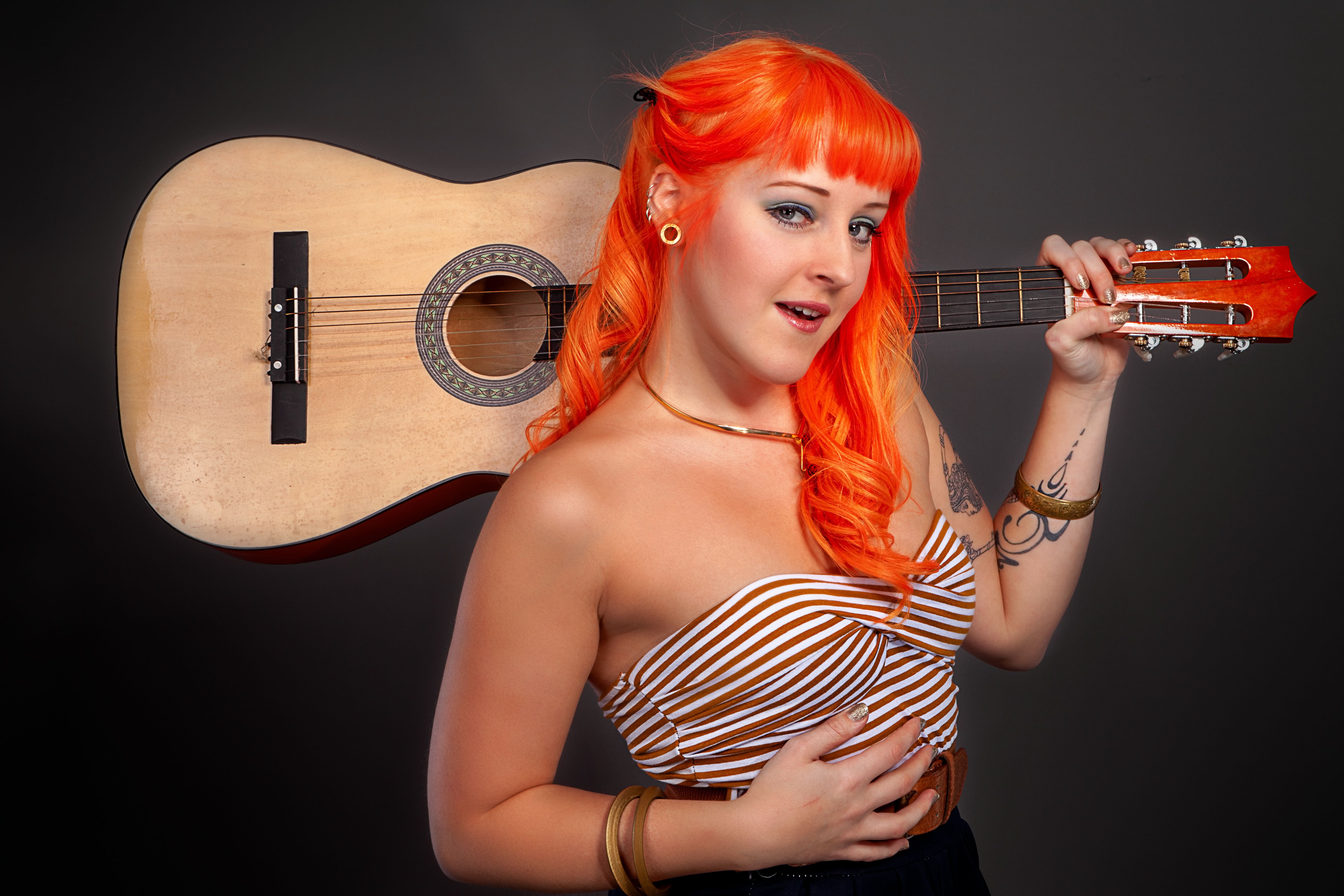 Portrait of a woman with orange hair holding a guitar in a studio setting.
