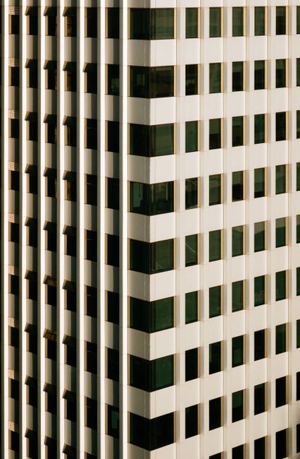 Background of high rise building with rows of white panels and windows in daylight