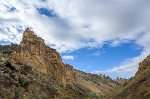 Rough stony terrain of peak among mountains under bright blue sky with cumulus clouds