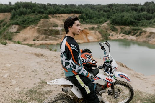 A motocross rider on a dirt bike at a scenic hillside quarry, gazing into the distance.