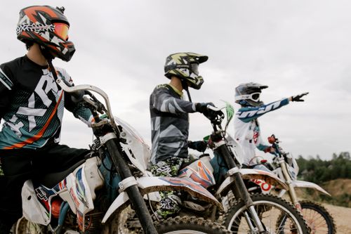 Free Three motocross riders in gear ready to race on dirt bikes outdoors. Stock Photo