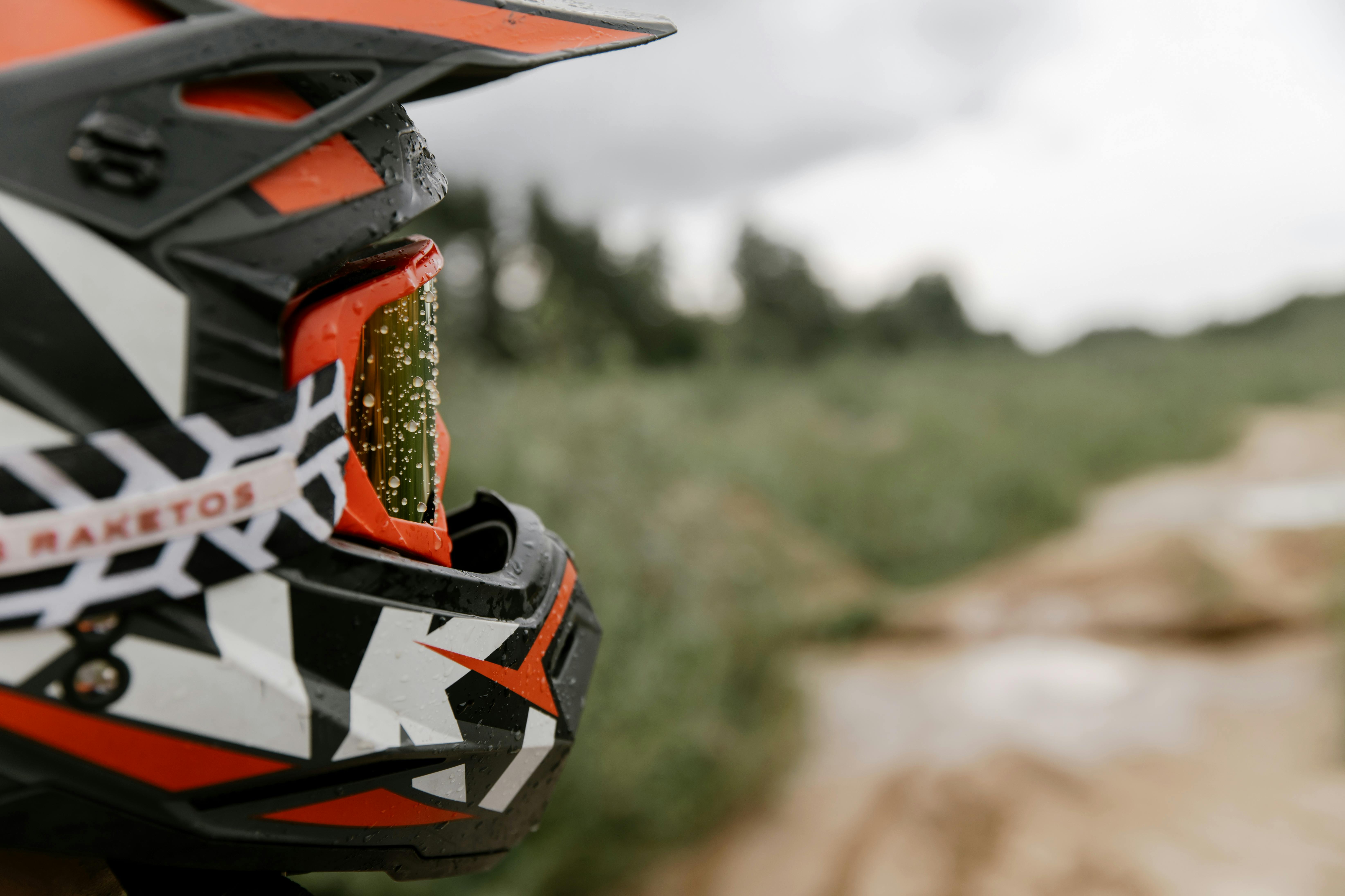 Close-up of motorcycle helmet with visor in outdoor setting, featuring rain droplets.