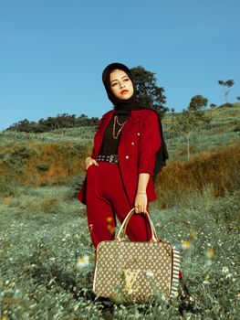 一位身着红衣的时尚女子在风景秀丽的草地上摆出姿势，尽显优雅与风格