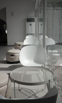A modern minimalist seating area with white chairs, glass panels, and air conditioning units.