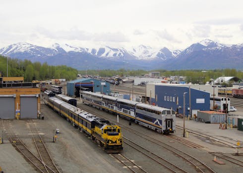 Anchorage train yard with snow-capped mountains and parked trains, Alaska.