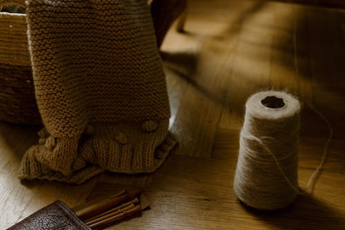 Handmade knitted blanket on wicker basket near needles and spool of thread