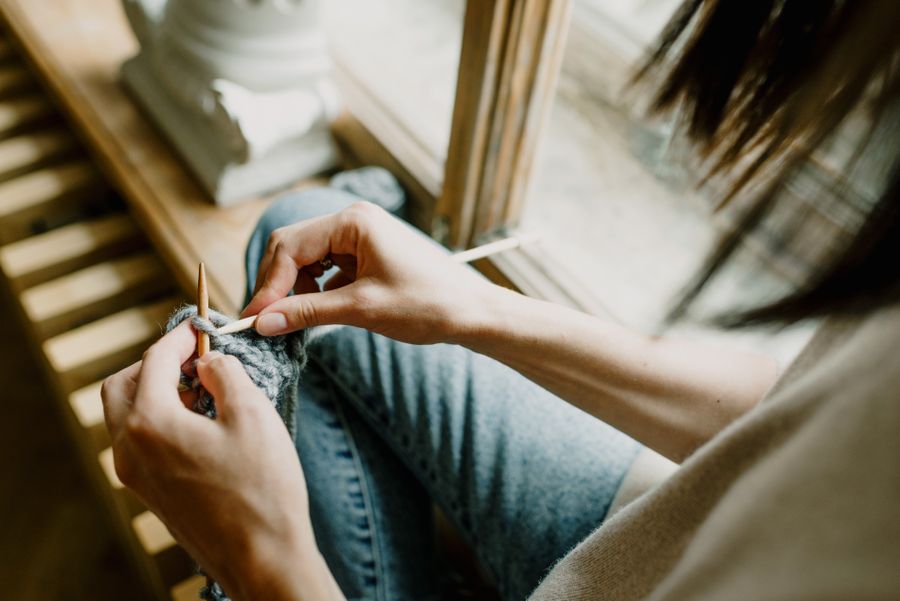 A woman knitting a garment by a bright window