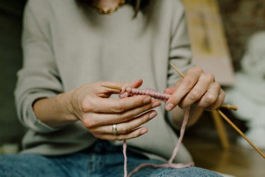 A person is knitting with pink yarn, showcasing the craft and texture in detail.