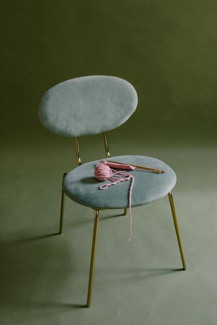 A stylish green chair featuring yarn and knitting needles on its seat, ideal for craft enthusiasts.